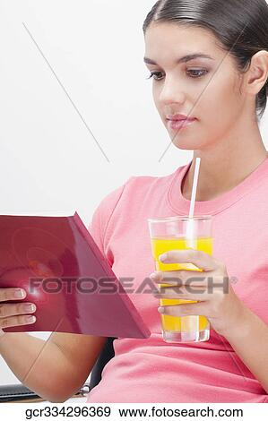 Stock Photo - Woman reading a book and with a glass of orange juice. Fotosearch