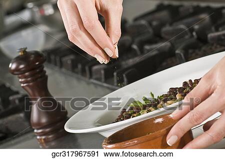 Stock Image - Woman sprinkling cilantro to beans. Fotosearch