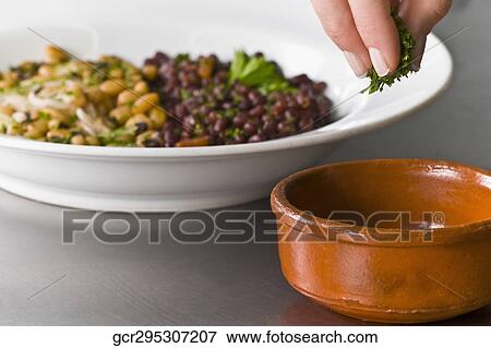 Stock Photo - Woman sprinkling cilantro to beans. Fotosearch