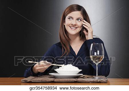 Picture - Woman talking on a mobile phone and eating rice. Fotosearch