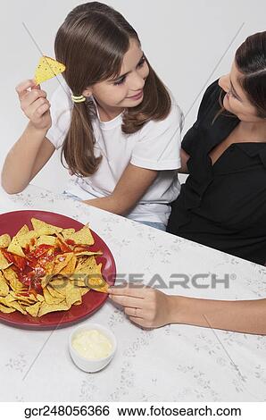 Woman with her daughter eating nachos with salsa View Large Photo Image Stock Photograph - Woman with her daughter eating nachos with salsa. Fotosearch