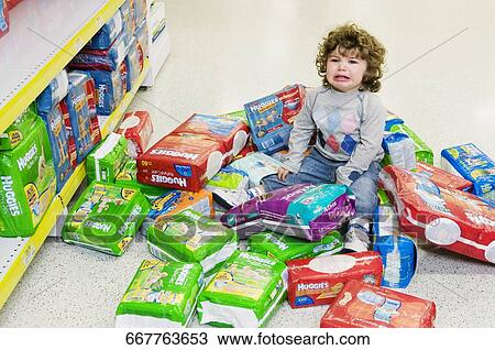 Stock Image - Baby boy crying with a heap of diapers around him. Fotosearch