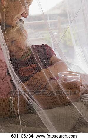 Picture - Baby girl holding a glass of water and sitting with her mother. Fotosearch