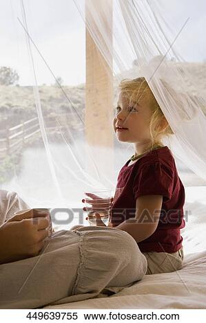 Stock Photography - Baby girl holding a glass of water and sitting with her mother. Fotosearch