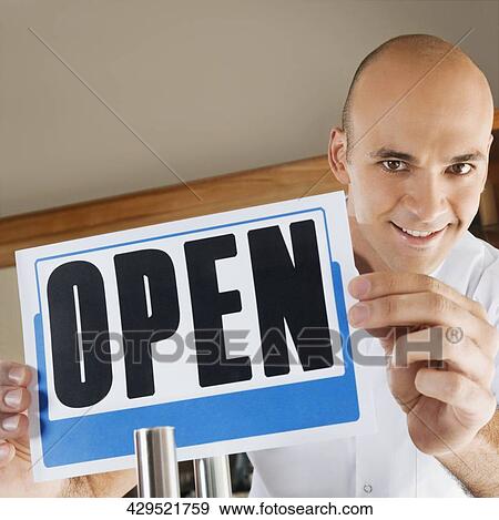 Stock Photo - Barber holding an Open signboard and smiling. Fotosearch