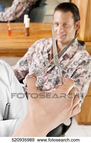 Stock Photo - Barber holding scissors with a man in the background. Fotosearch