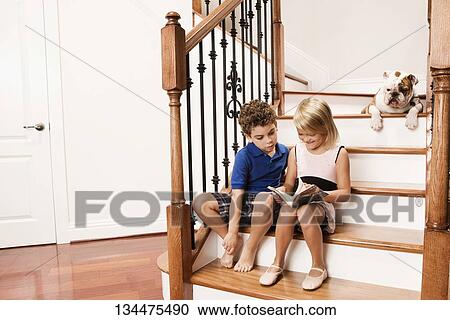 Stock Image - Boy and a girl sitting on a staircase and reading a book. Fotosearch