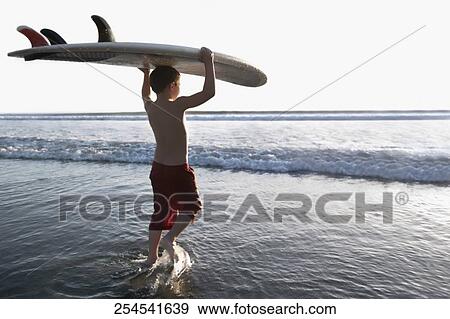 Stock Photo - Boy carrying a surfboard on the beach. Fotosearch