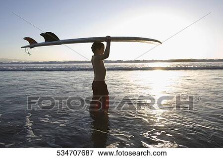 Stock Photo - Boy carrying a surfboard on the beach. Fotosearch