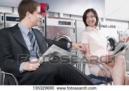 Stock Image - Businessman and a woman reading newspapers in a laundromat. Fotosearch