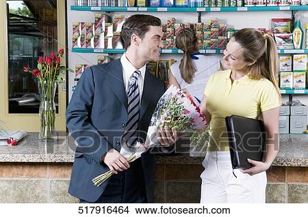 Businessman holding a bouquet of flowers with a woman standing beside him View Large Photo Image Picture - Businessman holding a bouquet of flowers with a woman standing beside him. Fotosearch