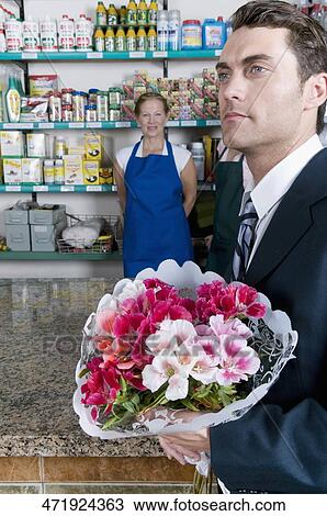 Businessman holding a bouquet of flowers with a female florist in the background View Large Photo Image Stock Image - Businessman holding a bouquet of flowers with a female florist in the background. Fotosearch