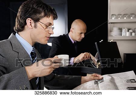 Stock Image - Businessman holding a cup of tea and reading a newspaper. Fotosearch