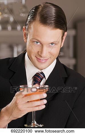Businessman holding a glass of cocktail and smiling View Large Photo Image Stock Image - Businessman holding a glass of cocktail and smiling. Fotosearch