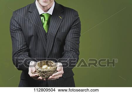 Businessman holding a golden egg in a nest View Large Photo Image Picture - Businessman holding a golden egg in a nest. Fotosearch