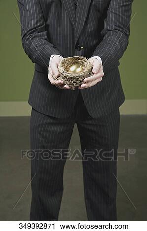 Businessman holding a golden egg in a nest View Large Photo Image Stock Image - Businessman holding a golden egg in a nest. Fotosearch