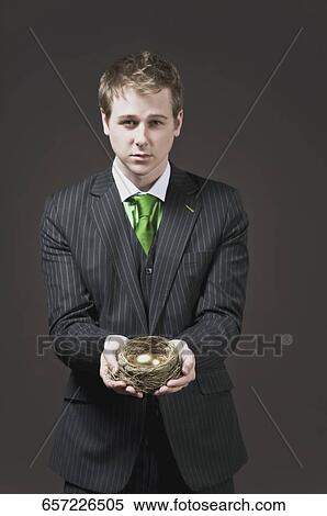 Businessman holding a golden egg in a nest View Large Photo Image Stock Photography - Businessman holding a golden egg in a nest. Fotosearch