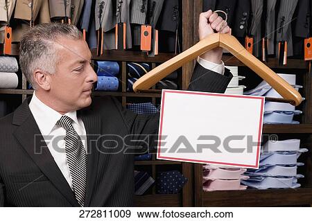 Businessman holding a hanger with blank signboard in a clothing store View Large Photo Image Stock Photo - Businessman holding a hanger with blank signboard in a clothing store. Fotosearch