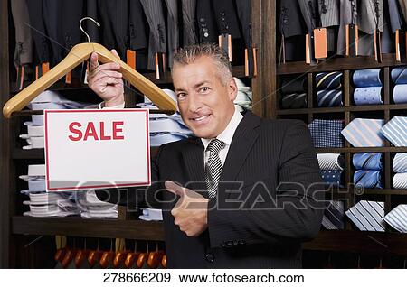 Stock Photo - Businessman holding a Sale sign in a clothing store. Fotosearch