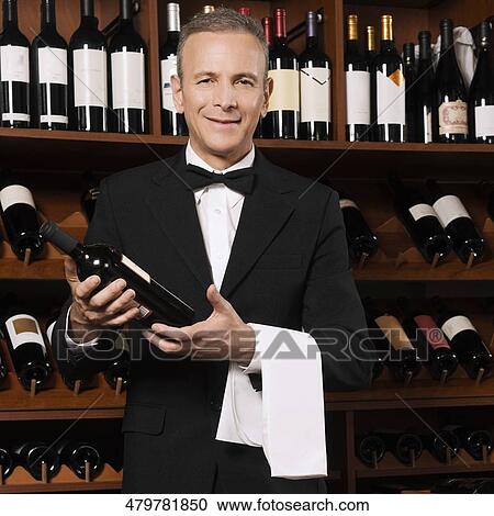 Stock Image - Businessman holding a wine bottle in a bar. Fotosearch