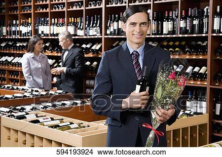 Picture - Businessman holding a wine bottle with a bouquet of flowers. Fotosearch