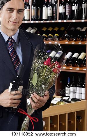 Stock Image - Businessman holding a wine bottle with a bouquet of flowers. Fotosearch