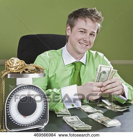 Businessman holding currency notes with gold jewelry on a weight scale in front of him View Large Photo Image Picture - Businessman holding currency notes with gold jewelry on a weight scale in front of him. Fotosearch