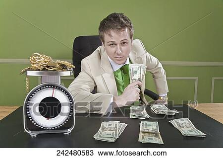 Businessman holding currency notes with gold jewelry on a weight scale in front of him View Large Photo Image Stock Image - Businessman holding currency notes with gold jewelry on a weight scale in front of him. Fotosearch