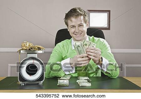 Businessman holding currency notes with gold jewelry on a weight scale in front of him View Large Photo Image Stock Image - Businessman holding currency notes with gold jewelry on a weight scale in front of him. Fotosearch