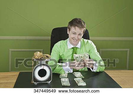 Businessman holding currency notes with gold jewelry on a weight scale in front of him View Large Photo Image Stock Photo - Businessman holding currency notes with gold jewelry on a weight scale in front of him. Fotosearch