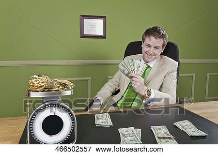 Businessman holding currency notes with gold jewelry on a weight scale in front of him View Large Photo Image Stock Photo - Businessman holding currency notes with gold jewelry on a weight scale in front of him. Fotosearch