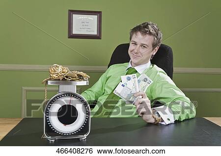 Businessman holding currency notes with gold jewelry on a weight scale in front of him View Large Photo Image Stock Photograph - Businessman holding currency notes with gold jewelry on a weight scale in front of him. Fotosearch