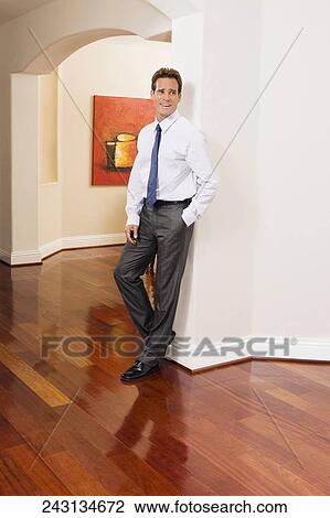Stock Image - Businessman leaning against a wall in a house. Fotosearch