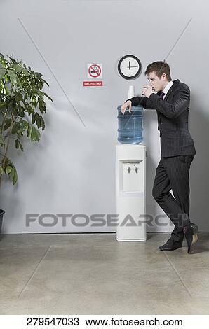 Businessman leaning on a water cooler and drinking water View Large Photo Image Stock Image - Businessman leaning on a water cooler and drinking water. Fotosearch