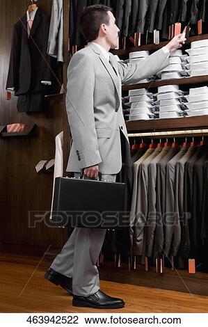 Businessman looking at coats in a clothing store View Large Photo Image Stock Image - Businessman looking at coats in a clothing store. Fotosearch