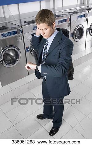 Businessman looking at wristwatch in a laundromat View Large Photo Image Stock Photo - Businessman looking at wristwatch in a laundromat. Fotosearch
