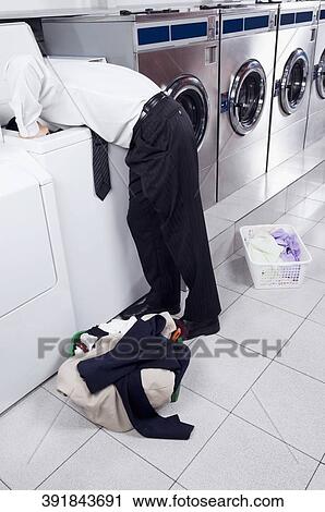 Businessman looking inside the washing machine in a laundromat View Large Photo Image Stock Image - Businessman looking inside the washing machine in a laundromat. Fotosearch