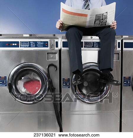 Businessman reading a newspaper in a laundromat View Large Photo Image Stock Image - Businessman reading a newspaper in a laundromat. Fotosearch