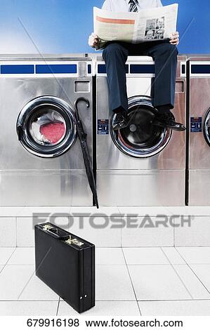 Businessman reading a newspaper in a laundromat View Large Photo Image Stock Photo - Businessman reading a newspaper in a laundromat. Fotosearch