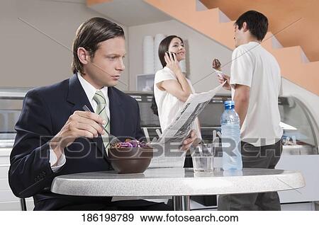 Stock Photo - Businessman reading a newspaper in an ice cream parlor. Fotosearch