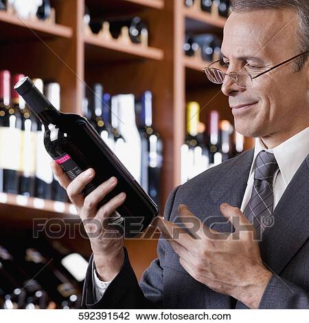 Stock Image - Businessman reading the label of a wine bottle. Fotosearch