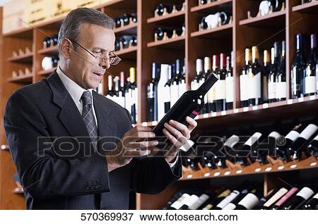 Businessman reading the label on a wine bottle View Large Photo Image Stock Photo - Businessman reading the label on a wine bottle. Fotosearch