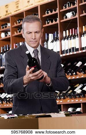 Stock Photo - Businessman reading the label on a wine bottle. Fotosearch