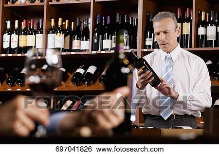 Stock Photograph - Businessman reading the label on a wine bottle. Fotosearch