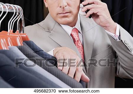 Businessman selecting a suit and talking on a mobile phone in a clothing store View Large Photo Image Stock Image - Businessman selecting a suit and talking on a mobile phone in a clothing store. Fotosearch
