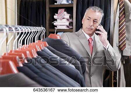 Businessman selecting a suit and talking on a mobile phone in a clothing store View Large Photo Image Stock Photo - Businessman selecting a suit and talking on a mobile phone in a clothing store. Fotosearch