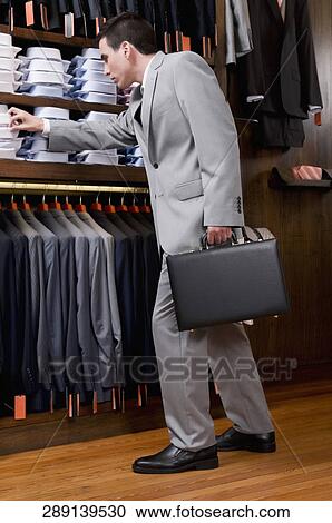 Stock Image - Businessman selecting shirts in a clothing store. Fotosearch