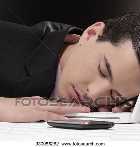 Stock Image - Businessman sleeping next to laptop. Fotosearch