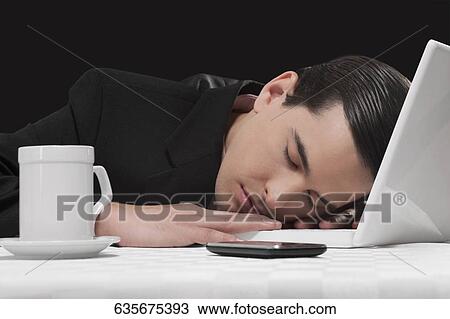 Stock Image - Businessman sleeping next to laptop. Fotosearch