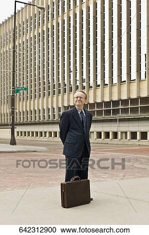 Stock Image - Businessman standing with hands behind back. Fotosearch